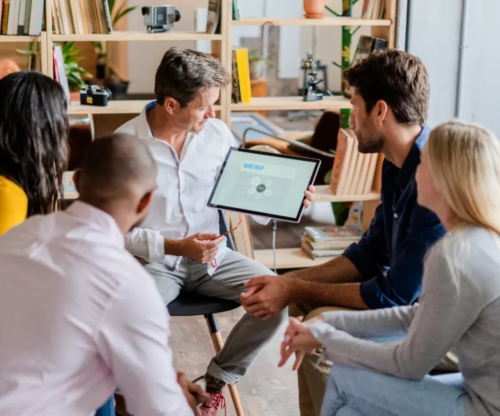 A team seated in a circle while a colleague shows them a tablet