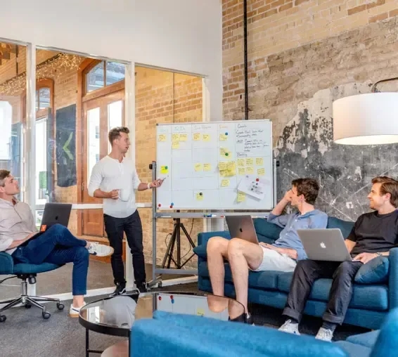 A team in a lounge area watching a colleague present notes on a whiteboard