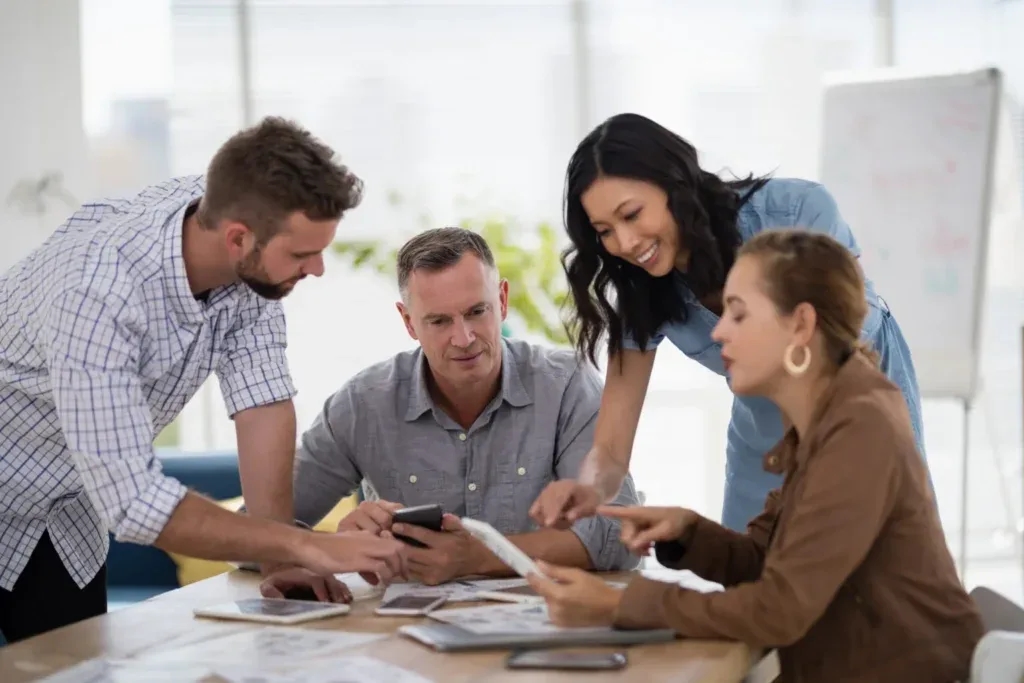 Four colleagues around a desk reviewing printed charts together